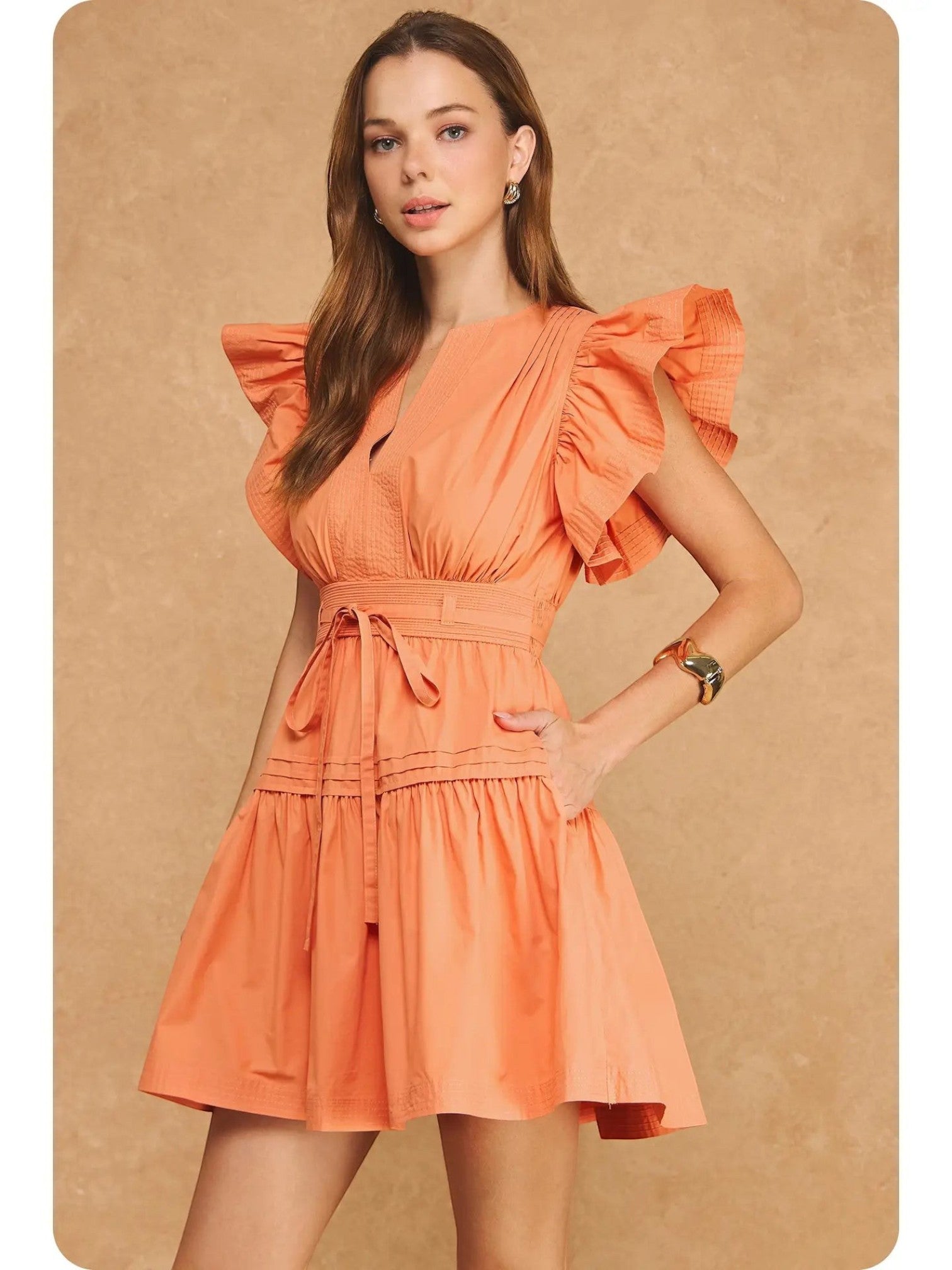 Mialur Valencia dress in cantaloupe orange with flutter sleeves, smocked waist, and tiered skirt on a female model