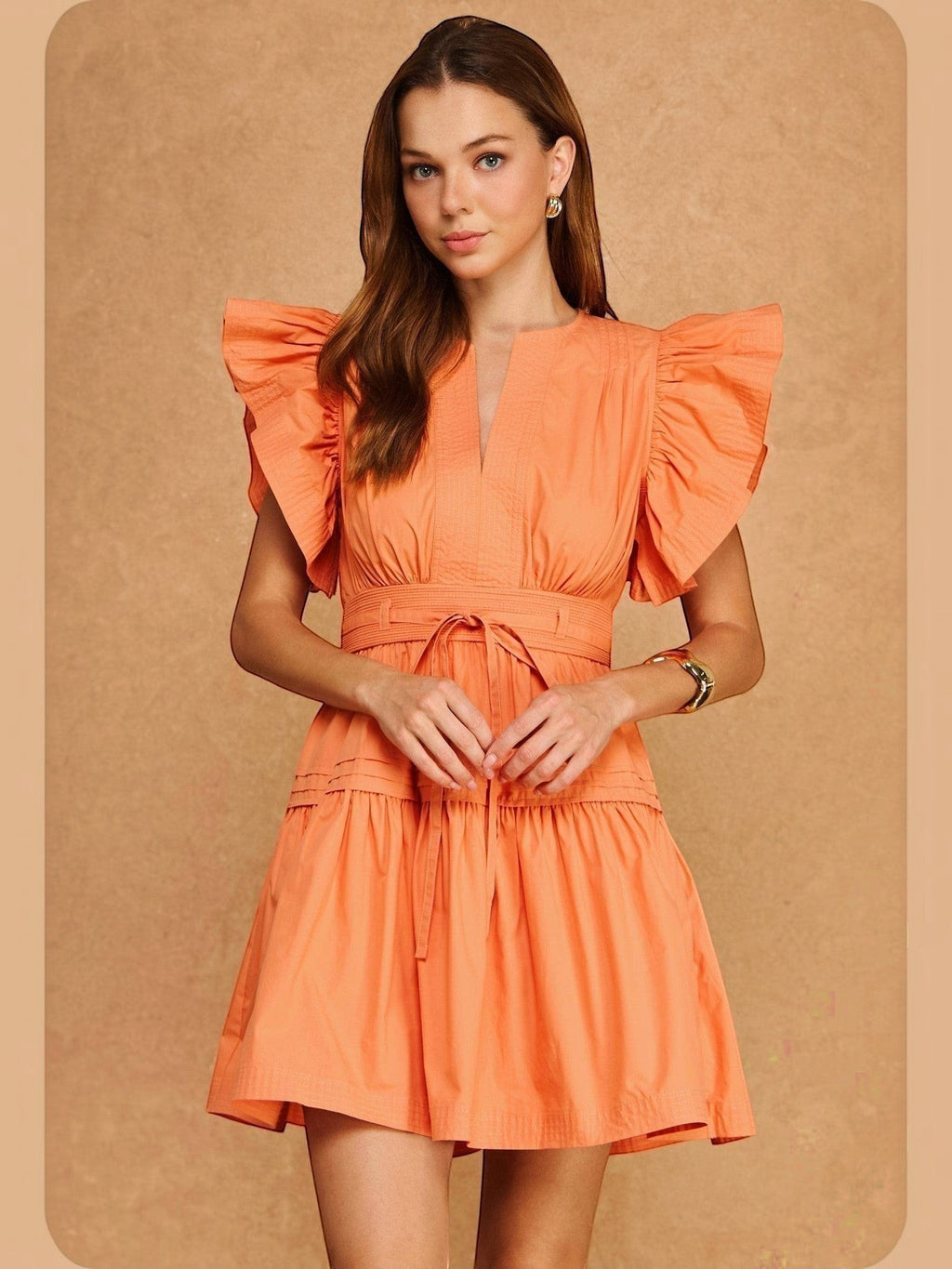 Mialur Valencia dress in cantaloupe orange with flutter sleeves, smocked waist, and tiered skirt on a model