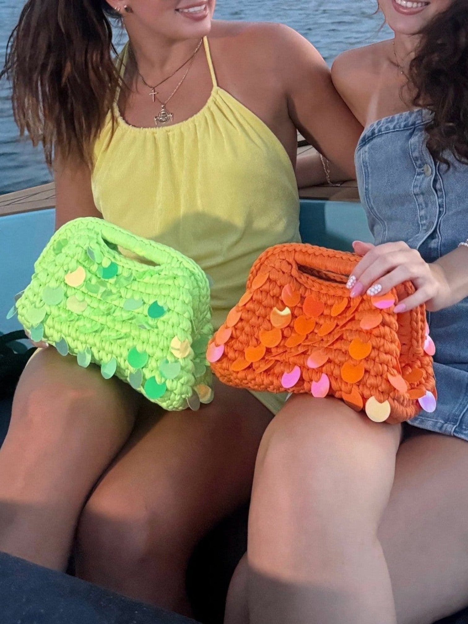 Mialur woven handbags in bright green and orange with iridescent paillettes held by two women on a boat