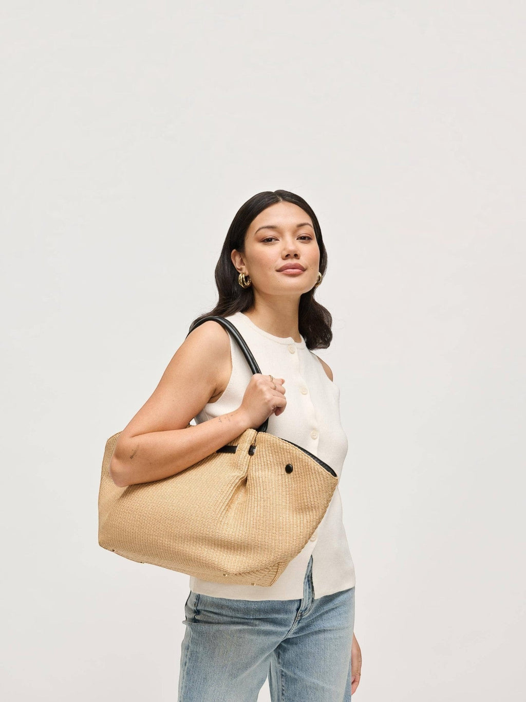 Mialur Summer Tote Bag in natural woven straw with black handles and gold-tone bow clasp carried by a woman