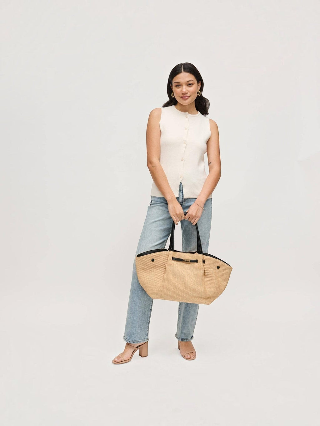 Model holding a Mialur woven straw tote bag with black handles and a gold-tone bow clasp against a white background.