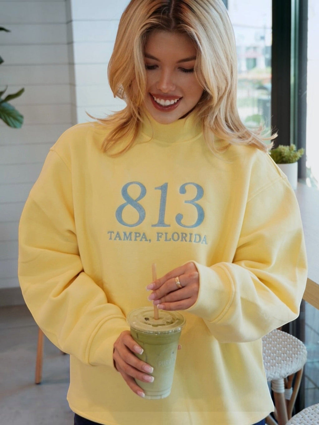 Mialur yellow cotton-blend mock neck sweatshirt with 813 Tampa Florida graphic worn by a smiling woman in a cafe