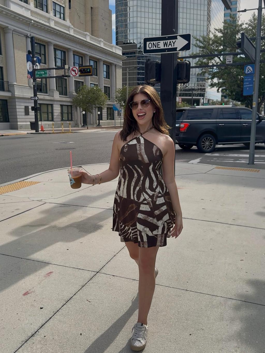 A woman wearing a Mialur mocha and cream zebra print satin halter mini dress with beaded detail walking in the city.
